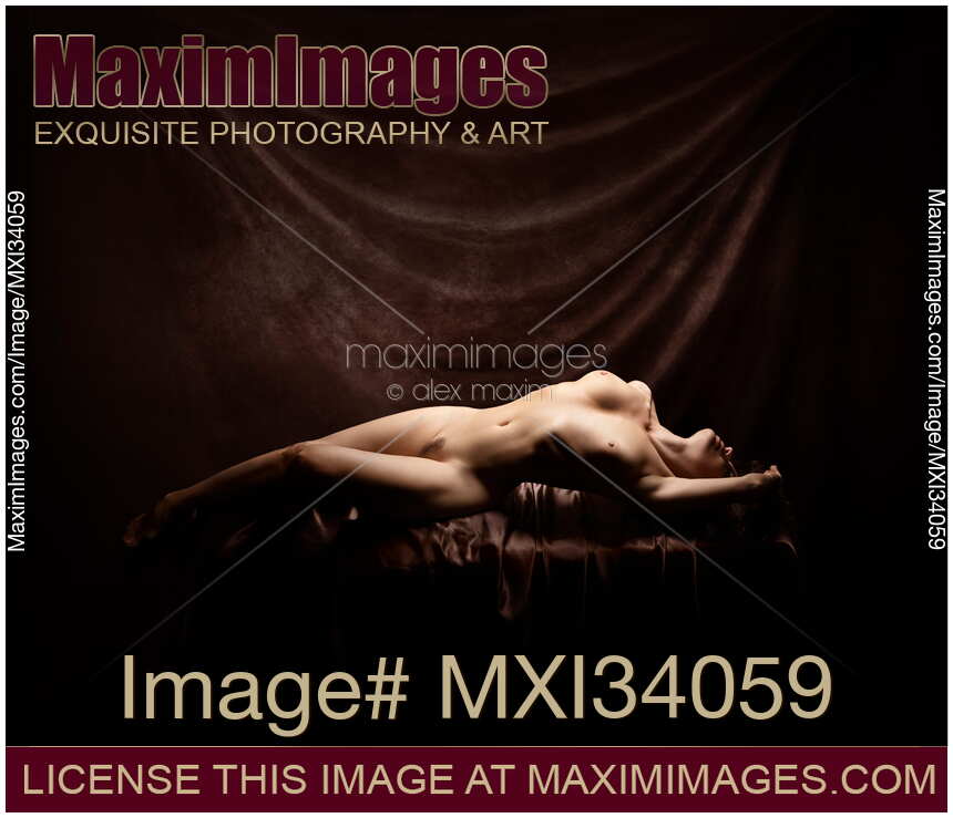 Fine art nude portrait of a beautiful woman lying naked in a sensual graceful pose in artist studio on dark background