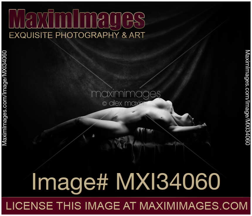 Fine art nude portrait of a beautiful woman lying naked in a sensual graceful pose in artist studio Black and white
