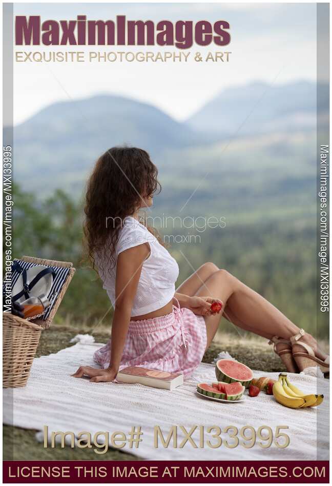 Girl sitting on a blanket with fruits and a book enjoying a little picnic in summer nature scenery