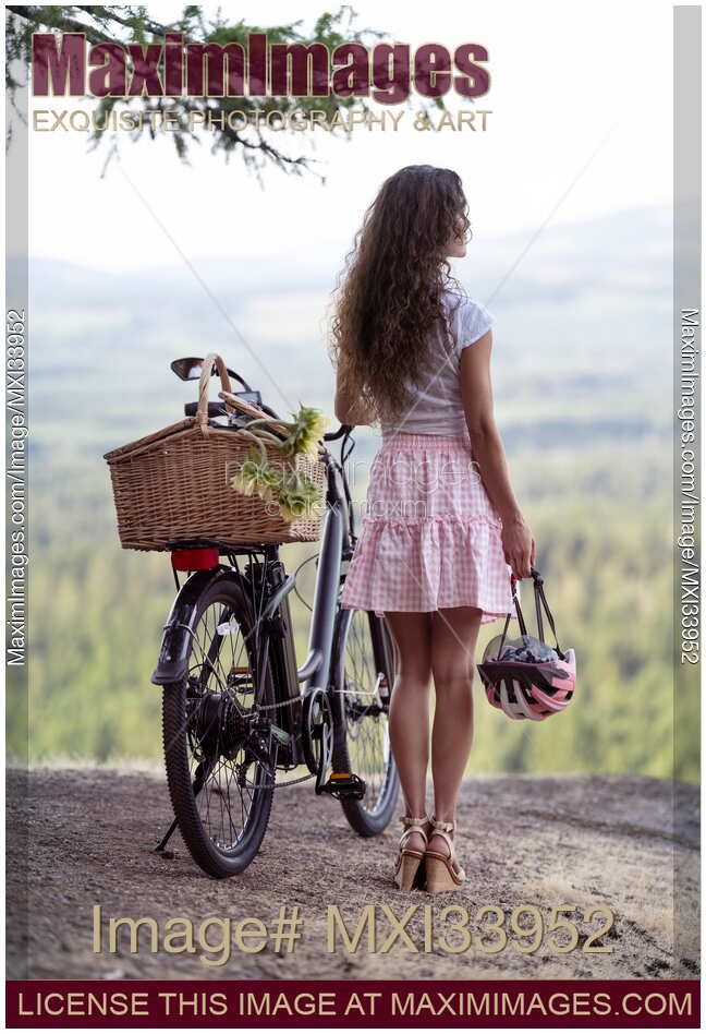 Girl with an electric bike and a pink bicycle helmet enjoying the nature view from a cliff
