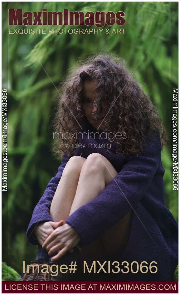 Girl with long curly hair and cute dreamy expression sitting in tranquil green forest nature scenery