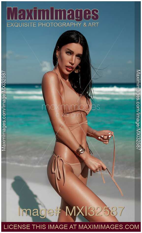 Glamorous sexy sun-tanned exotic woman in a bikini swimsuit posing on a sandy shore of Caribbean Sea beach
