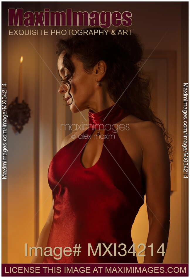 Gorgeous classy lady in sexy red dress standing in dim candle light with a contemplative look