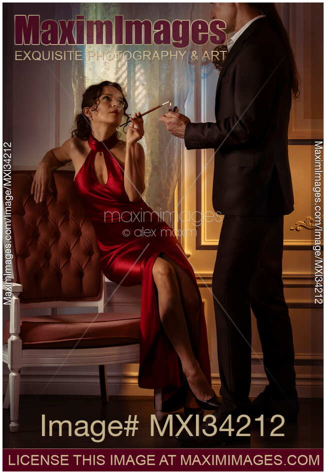 Gorgeous classy lady sitting on a chair and a gentleman lighting her cigarette