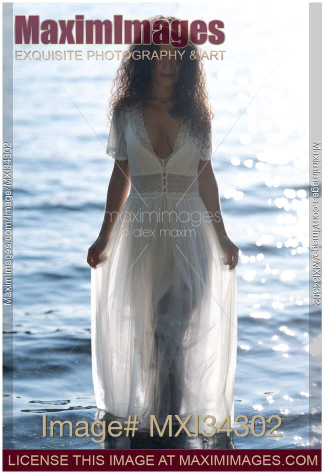 Gorgeous goddess-like woman in sheer white dress walking out of sea water in bright sunlight