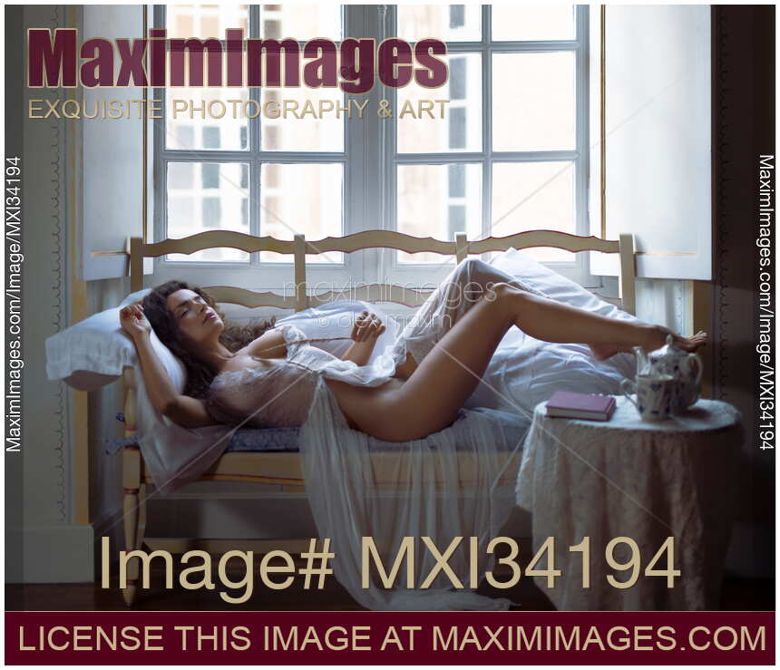 Gorgeous half naked woman in sheer white lace nightgown lying relaxed on antique sofa with a feather