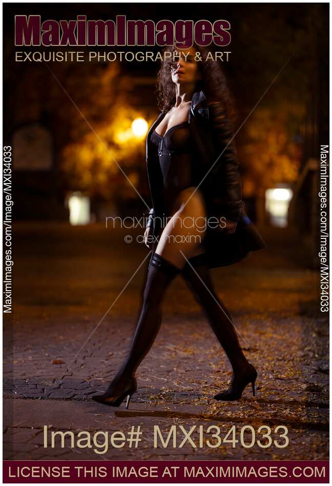 Gorgeous woman in black trench coat revealing sexy lingerie and stockings crossing a night city street