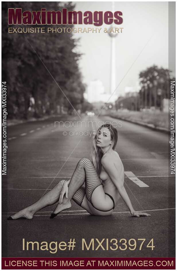 Half-nude woman in fishnet stockings sitting on the street asphalt. Black and white art nude portrait.