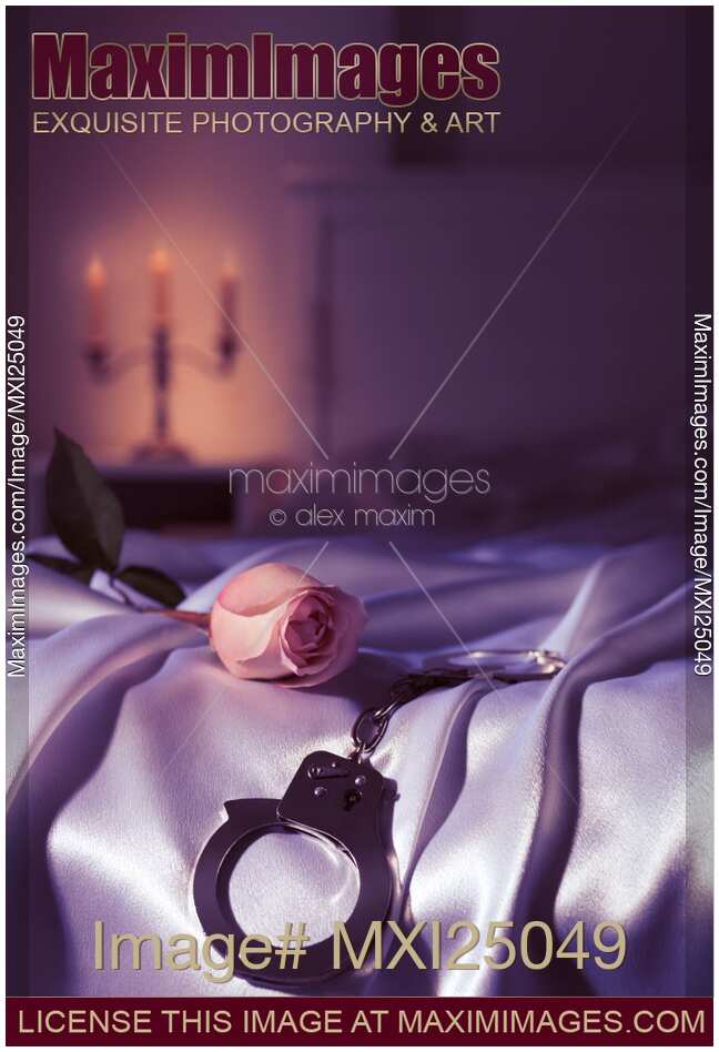 Handcuffs and a rose on bed. Suggestive intimate scene still life.
