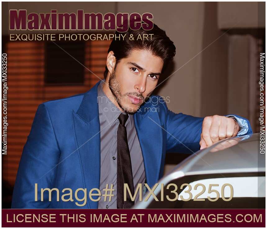 Handsome man in elegant blue suit leaning against a car