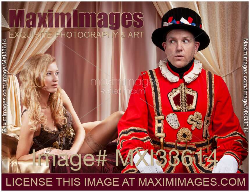 Humorous couple portrait of a Beefeater, Royal bodyguard and a beautiful sexy lady sitting on a bed