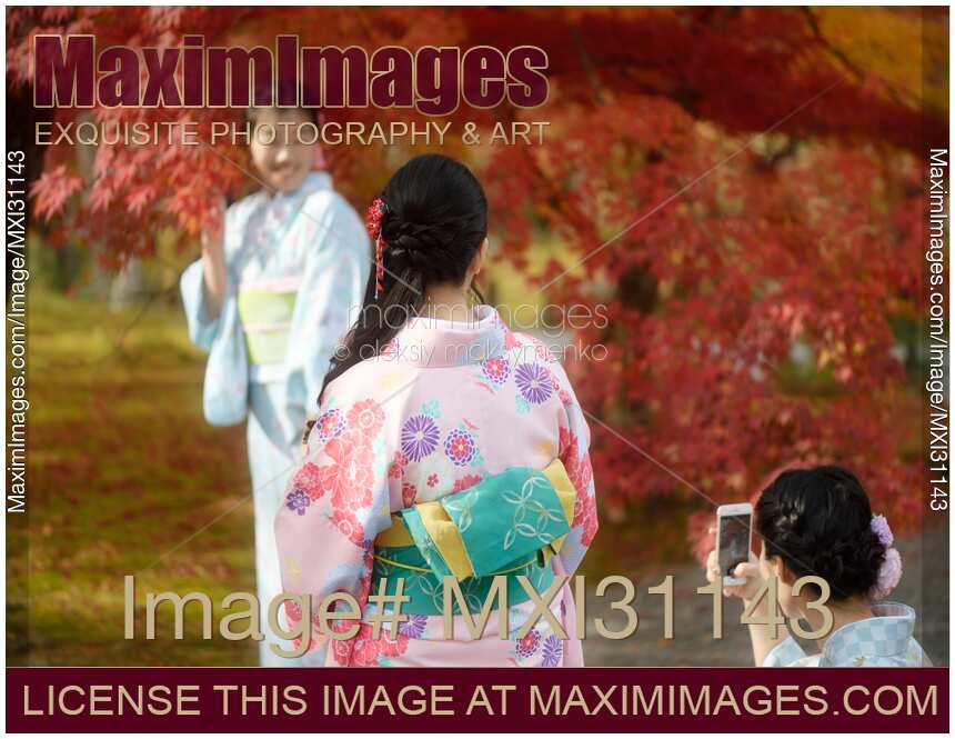 Japanese girls in colorful yukatas taking pictures in Kyoto autumn scenery
