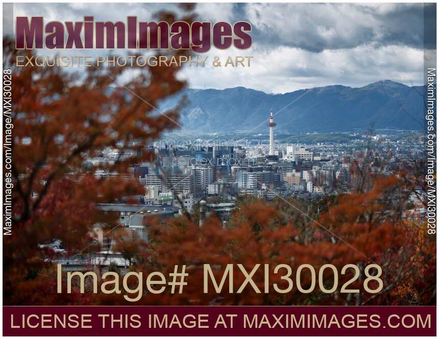 Kyoto tower under dramatic sky in aerial city scenery behind red autumn trees