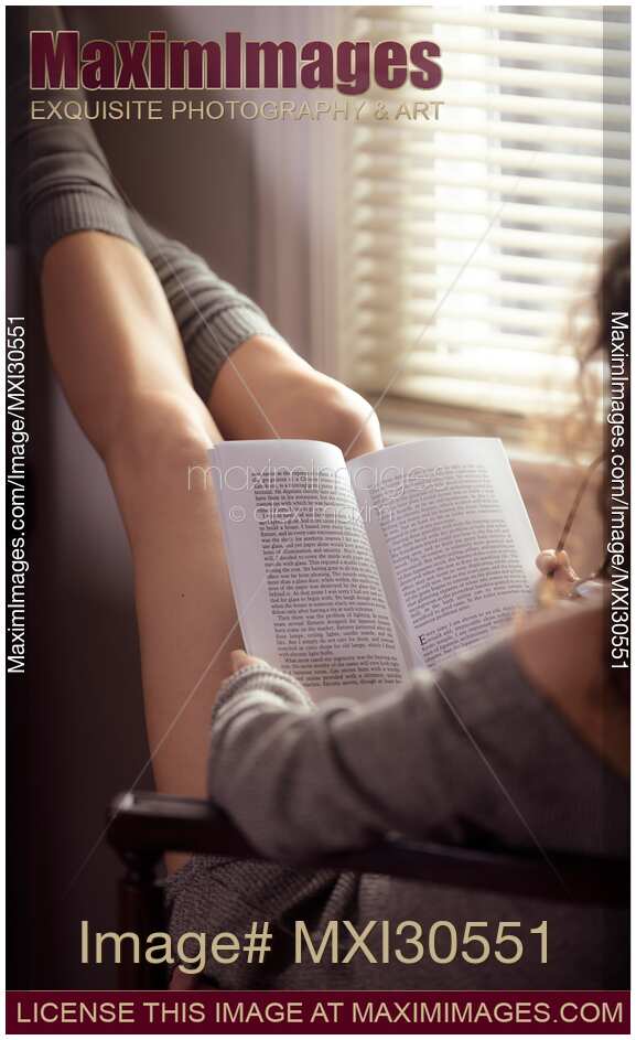 Legs of a woman reading a book in a chair by the window