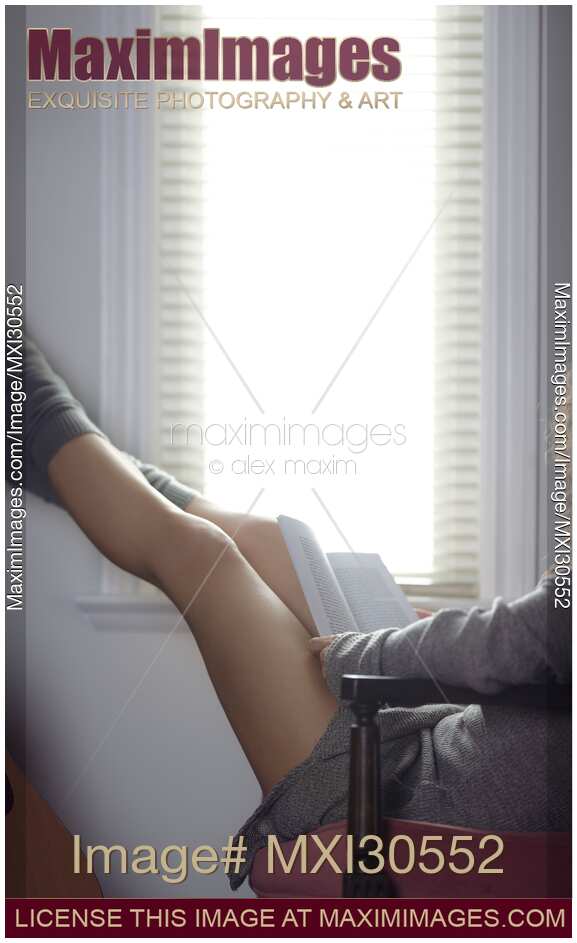 Legs of a woman sitting in a chair with a book reading by the window
