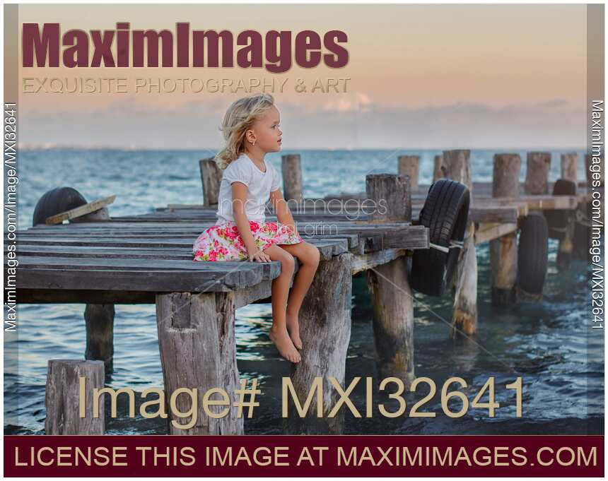 Little girl sitting on a wooden pier at the sea