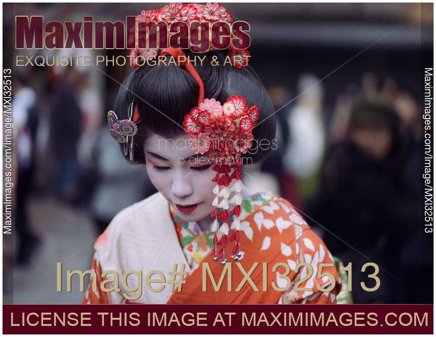Maiko apprentice Geisha beautiful face with white makeup and red Kanzashi hairpins in her wig bowing her head