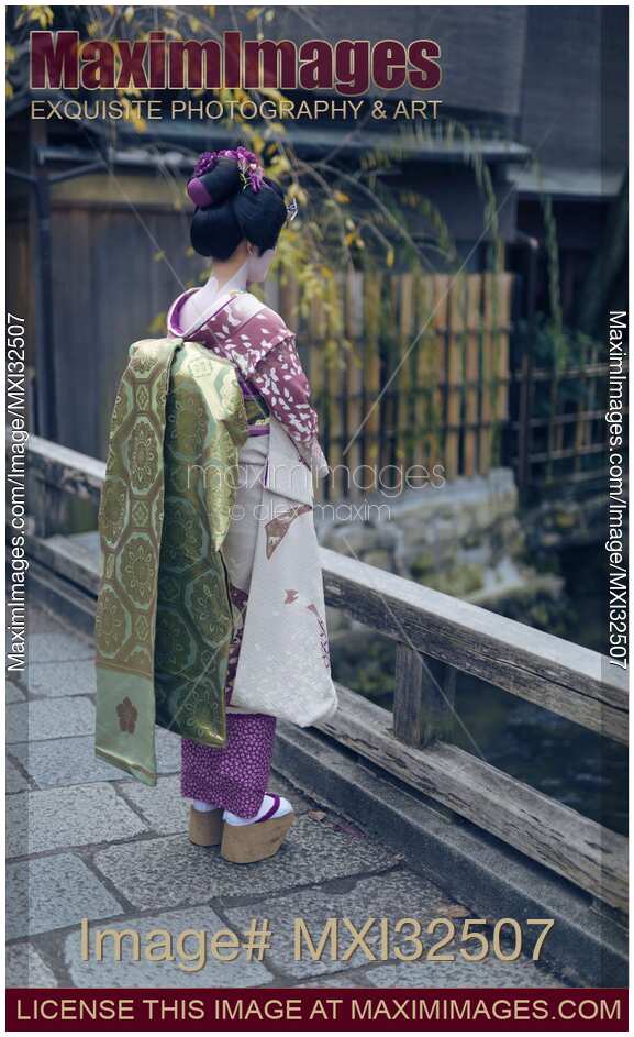 Maiko Geisha apprentice in kimono with long obi belt and okobo shoes alone on a bridge in Kyoto