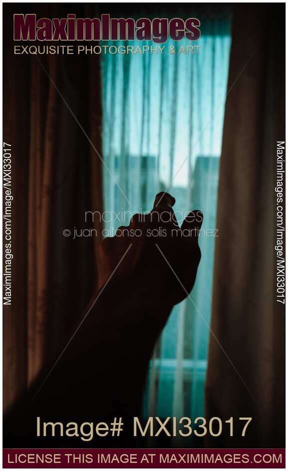 Male hand reaching towards the window from darkness of a house