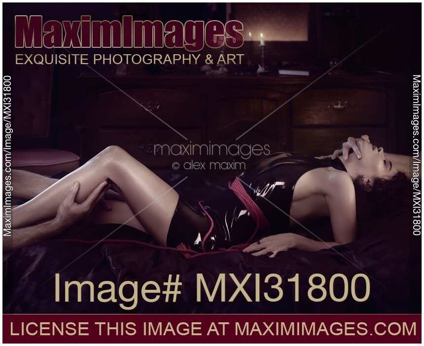 Male hands caressing a woman reclining on a bed in a sexy slick black leather dress and a rope around her body