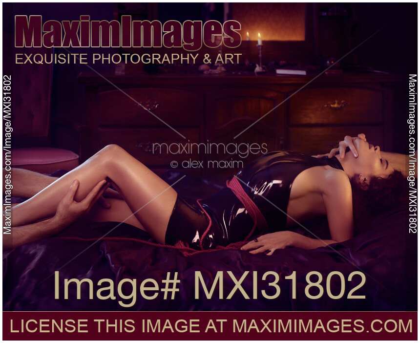 Male hands caressing a woman reclining on a bed in a sexy slick black pu leather dress and a rope tied around her body