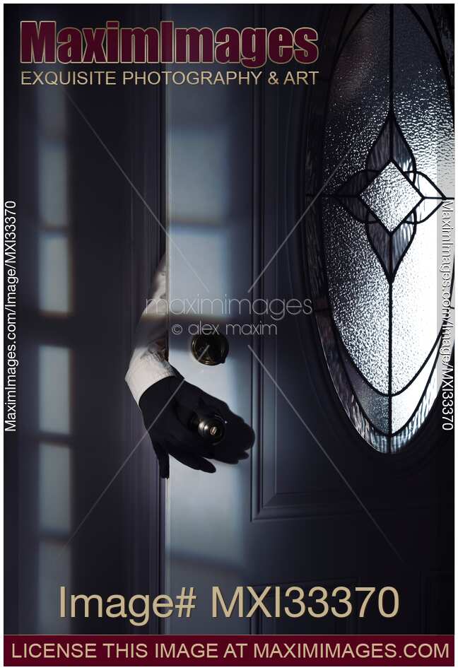 Man hand in a black gloves reaching for a door handle from behind a door in a dark shadowy house