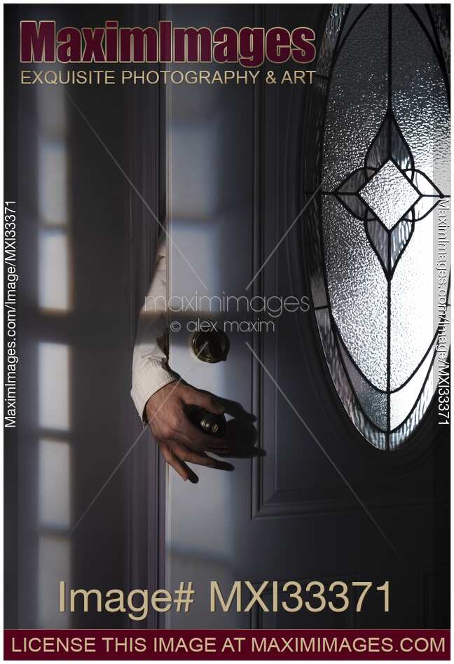 Man hand reaching for a door handle from behind a dark shadowy house entrance door