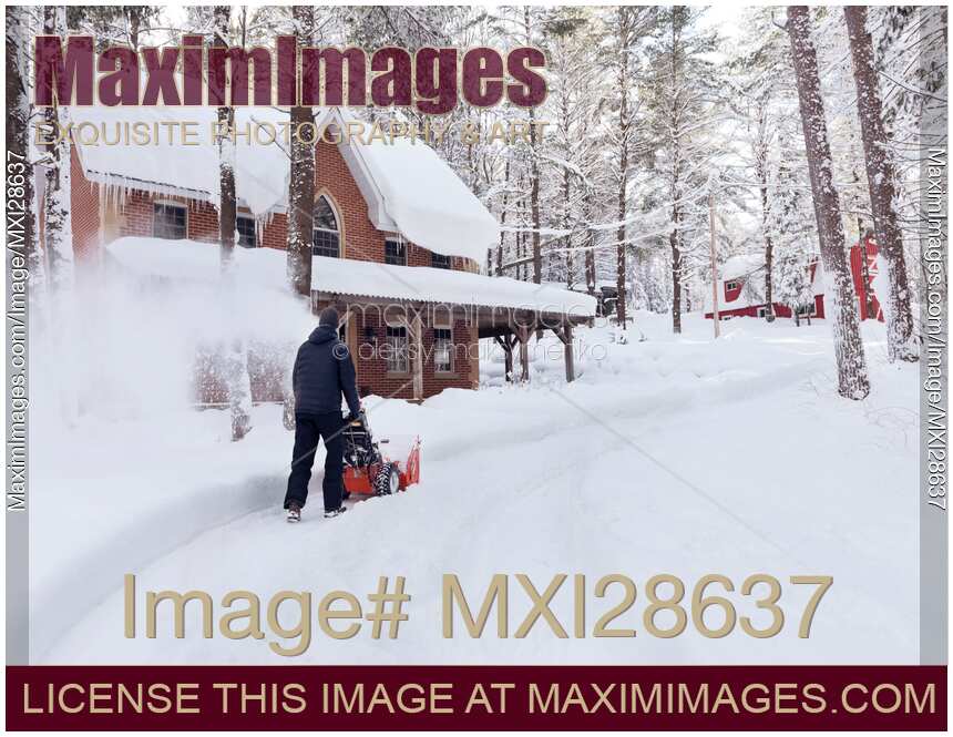 Man with snow thrower clearing driveway near house