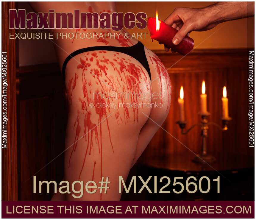 Melted red wax dripping from candle on sexy woman buttocks