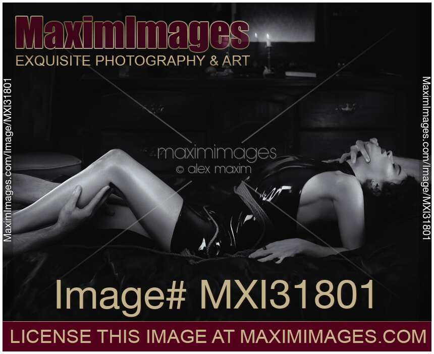 Men hands caressing a woman lying on a bed in sexy black leather dress and a rope around her body Black and white