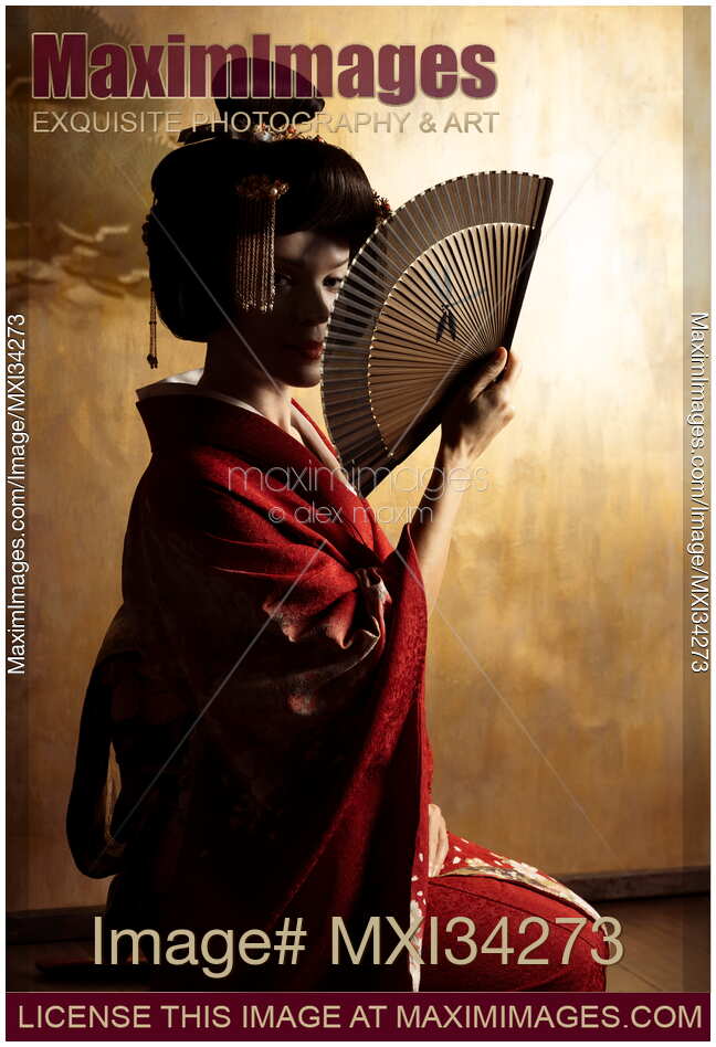Mesmerizing portrait of beautiful caucasian lady, Japanese geisha with hand fan casting shadows on her face against golden wall