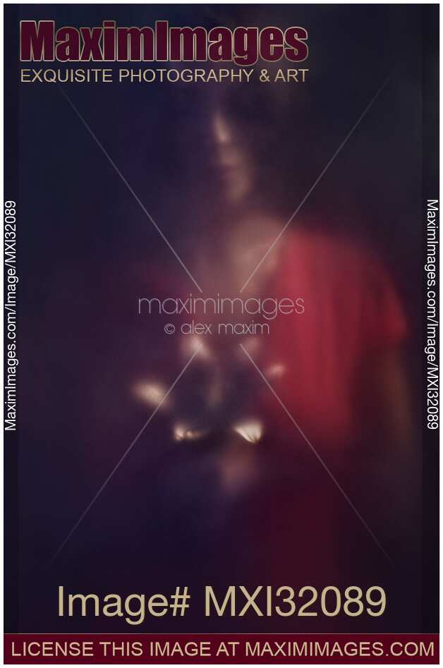 Mysterious dark portrait of a woman looking at a lily flower in her hands behind hazy glass in darkness