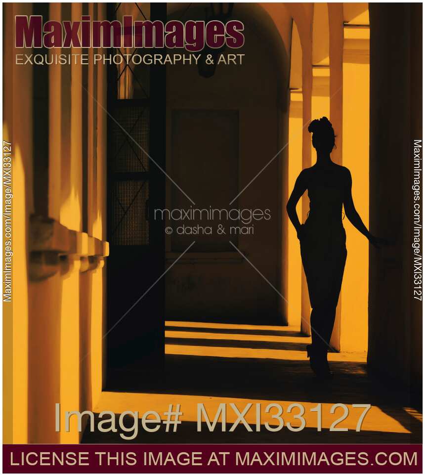 Mysterious dark silhouette of a woman walking in a shadowy arched hallway of an old building