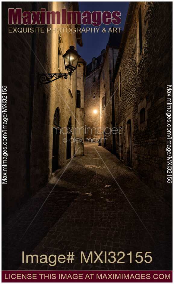 Narrow dark cobbled street with stone houses with street lamps at night in France