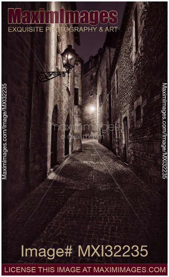 Narrow dark cobbled street with stone houses with street lamps at night in France Artistic black and white