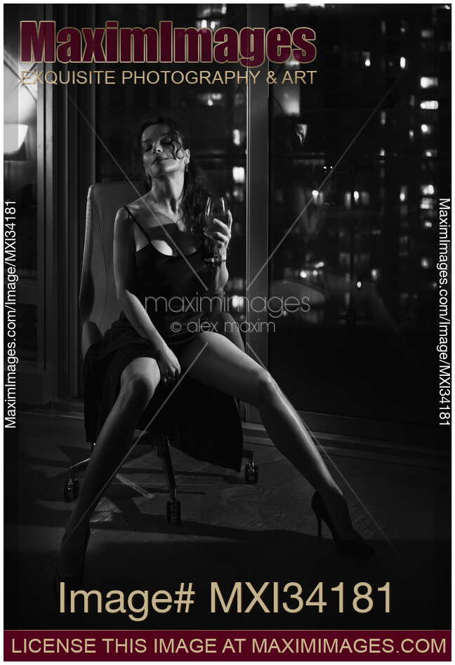 Noir portrait of a gorgeous lady sitting in chair in provocative pose by window with night city view