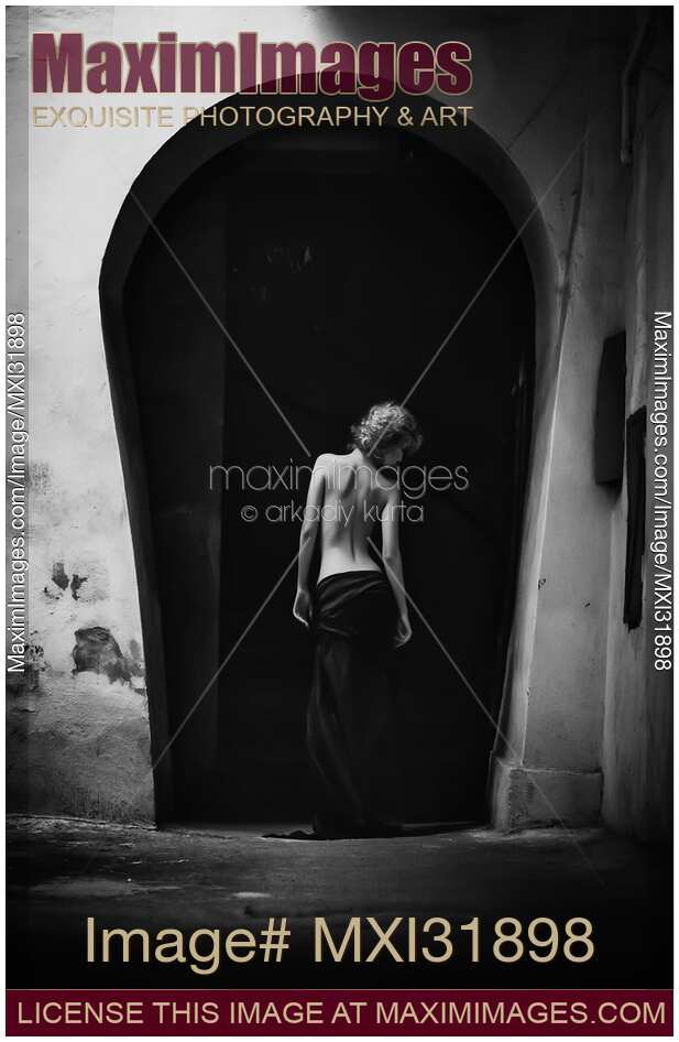 Nostalgic fine art portrait of a young woman standing with her back in an old archway