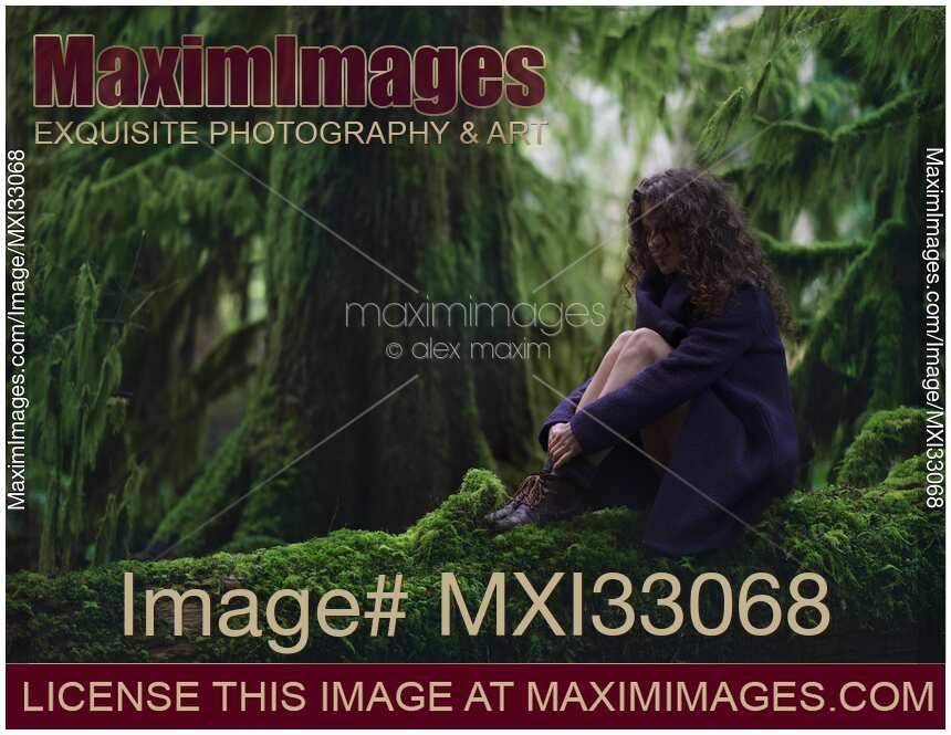 Nostalgic tranquil moody nature scenery of a woman sitting on mossy tree trunk in green forest scenery