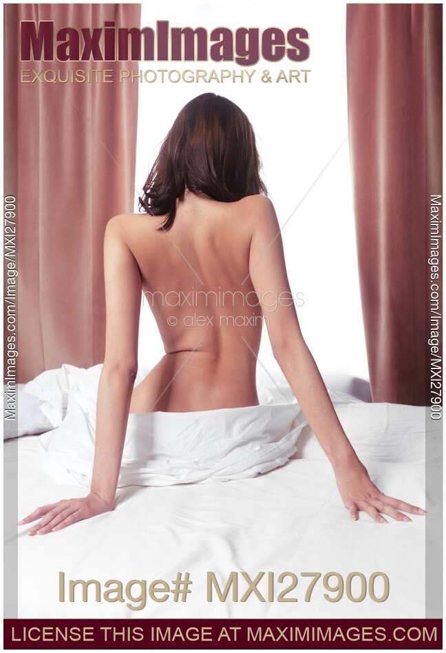 Nude back of woman sitting on bed in front of window