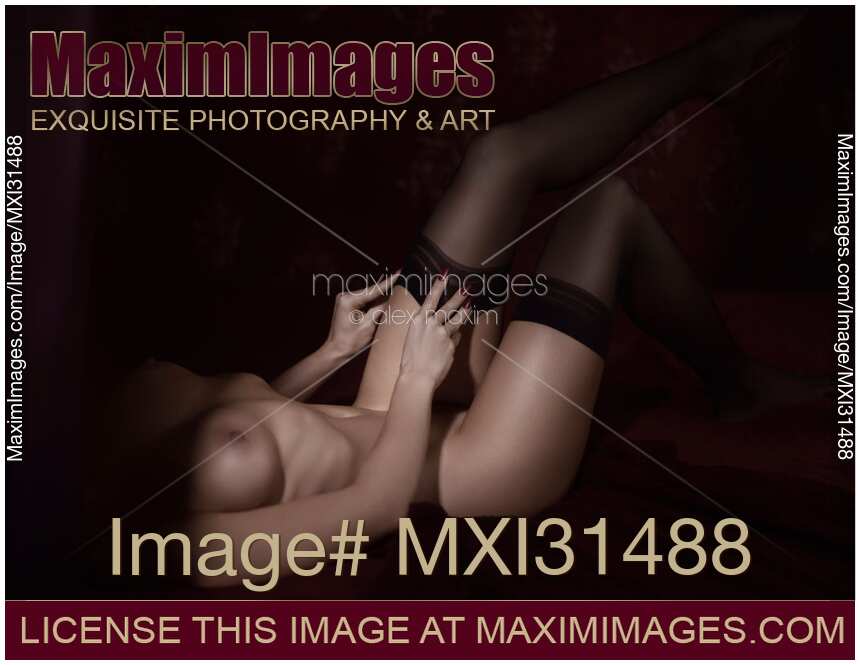 Nude woman lying in bed putting on black stockings abstract closeup of her naked body and legs