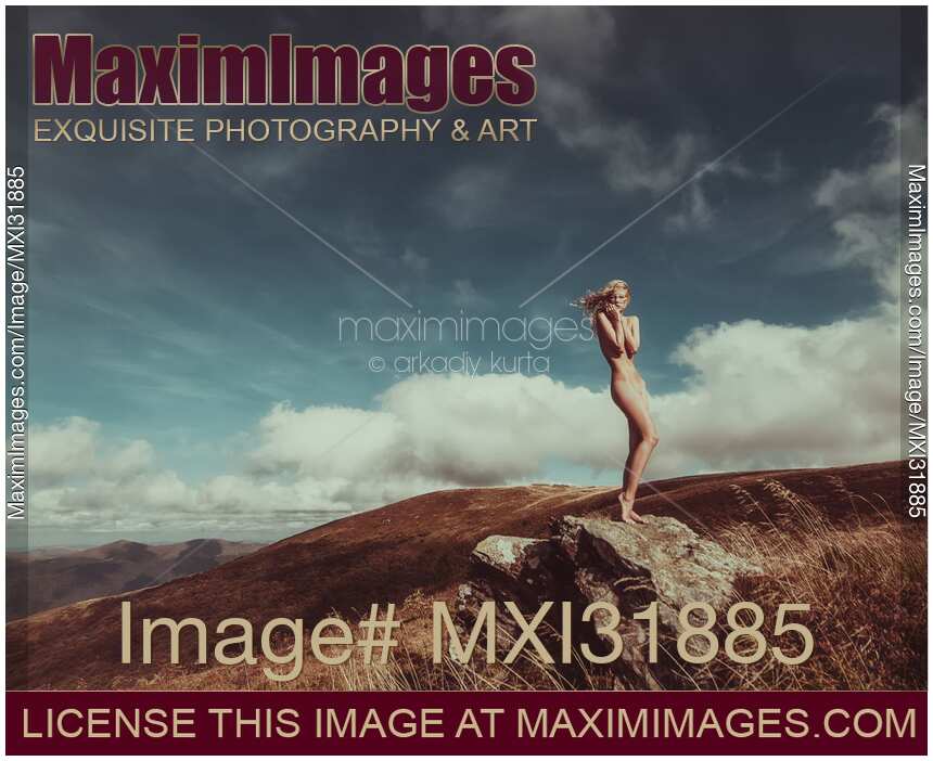 Nude woman standing gracefully on rocks in mountain landscape scenery with blue skies