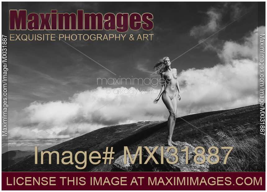 Nude woman standing on rocks in mountain landscape scenery wind blowing her blond hair
