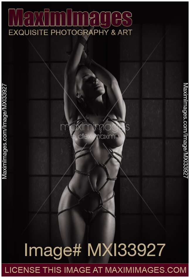 Nude woman standing with Shibari bondage ropes around her sensual naked body and hands tied above her head. Black and white.