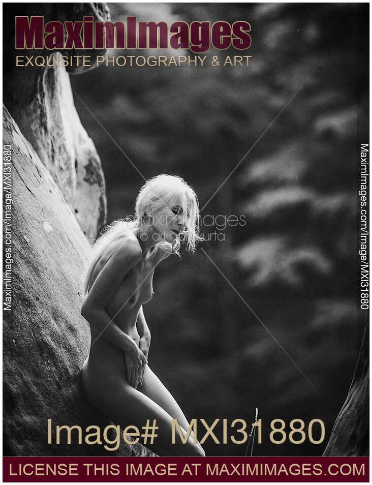 Nude woman with long white hair leaning against the rocks in the nature