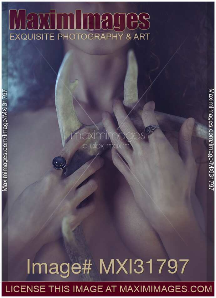 Ominous concept of beautiful mysterious woman holding deer antlers close to her bare chest