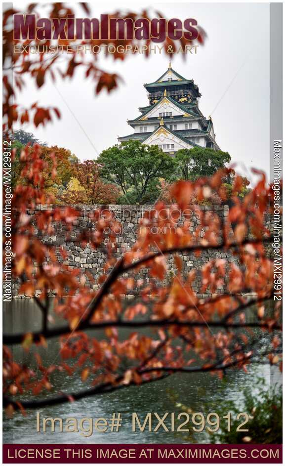 Osaka Castle and canal from behind red tree branches in autumn