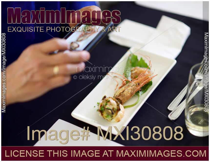 Person hands taking pictures of a gourmet seafood meal at a restaurant with a smartphone