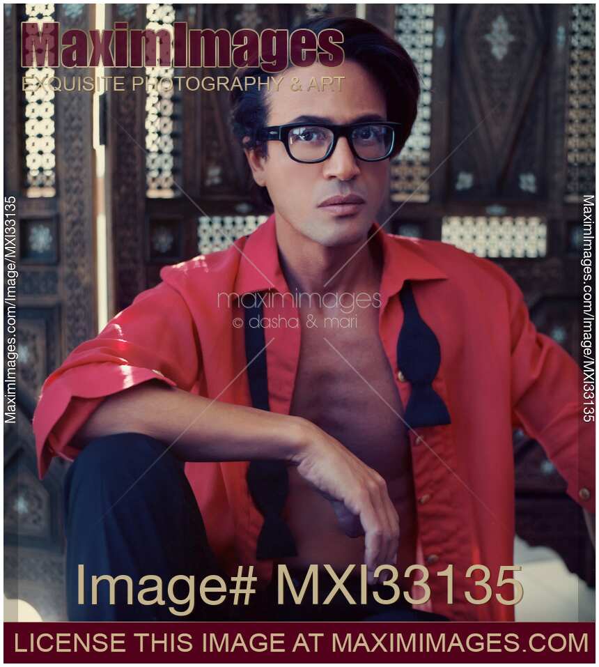 Portrait of a man in an undone stylish red shirt and glasses sitting relaxed in a retro style room