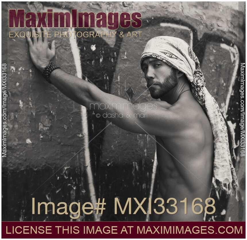 Portrait of a sexy handsome bearded man with bare torso wearing bandana leaning against graffiti wall Black and white