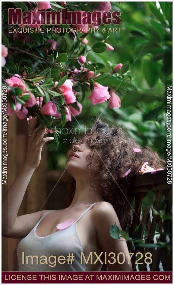 Portrait of a woman standing under a beautiful blooming camellia tree touching its pink flowers